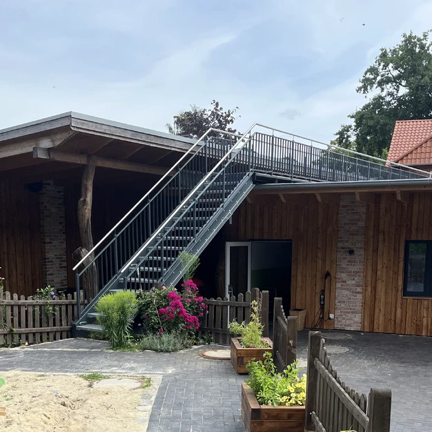 Modernes Holzhaus mit externer Metalltreppe und begrüntem Vorgarten