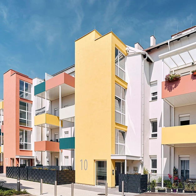 Moderne farbenfrohe Wohnhäuserreihe mit gelber Mitte und weiß-rosa Akzenten unter blauem Himmel