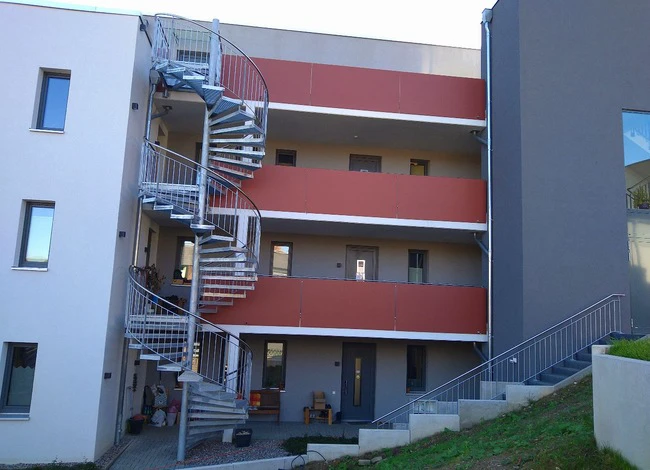 Modernes Apartmenthaus mit auffälliger Wendeltreppe und roten Akzentbändern an der Fassade