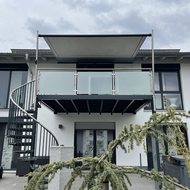 Moderne Architekturfassade mit schwarzer Treppe und Balkon teilweise verdeckt von grünen Zweigen
