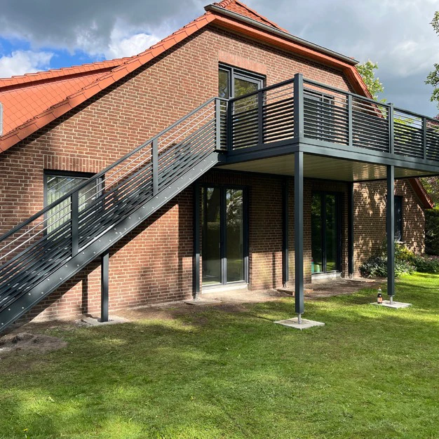 Backsteinhaus mit rotem Dach externer Metalltreppe und Veranda vor grünem Rasen