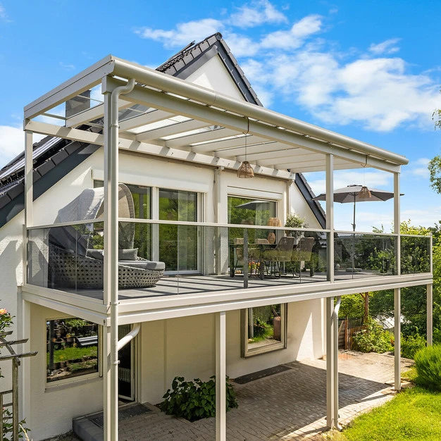 Moderne Villa mit überdachtem Balkon und heller Pergola an sonnigem Tag im Garten