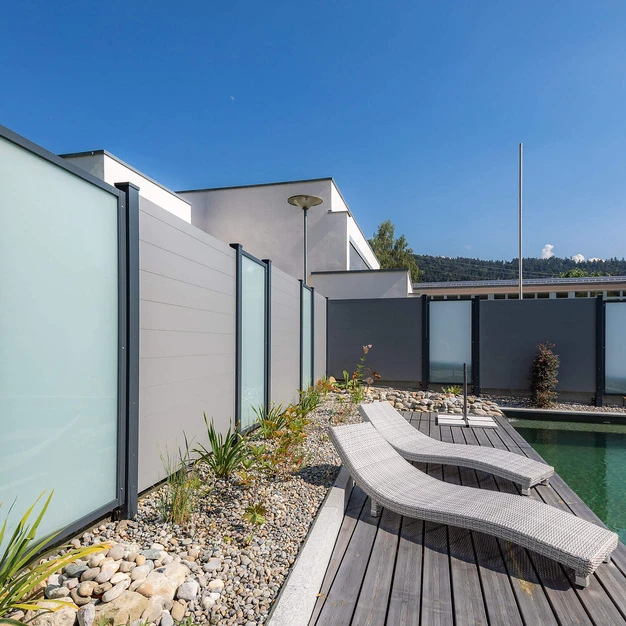Moderner Poolbereich mit Holzdeck zwei Liegen und architektonischen grauen Sichtschutzwänden