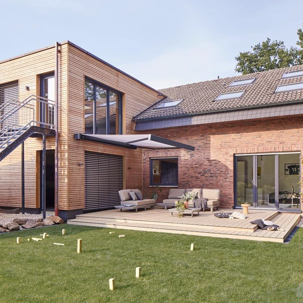 Modernes Haus aus Holz und Ziegeln mit großer Terrasse und Solaranlage vor einem gepflegten Rasen