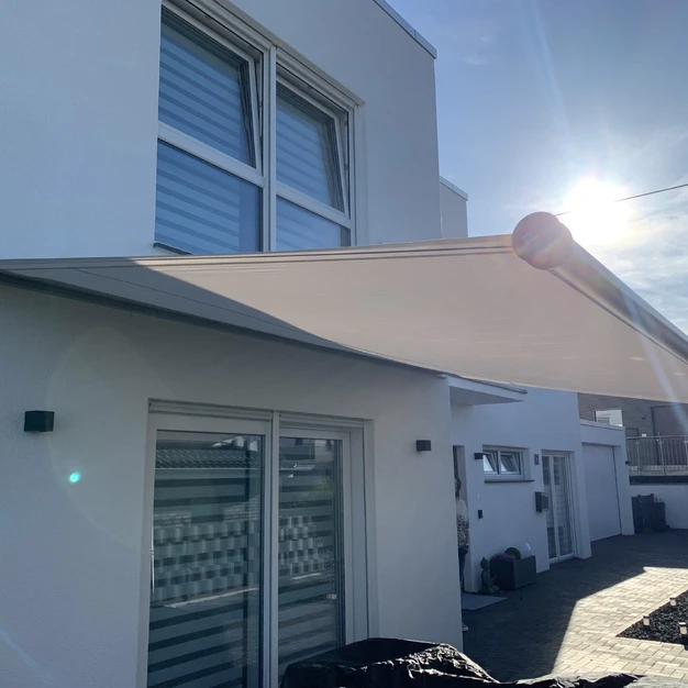 Modernes weißes Gebäude mit großen Fenstern und Sonnensegel vor hellem Sonnenlicht