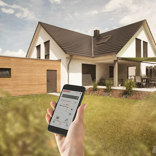 Smartphone mit Immobilienvisualisierung vor einem modernen weißen Einfamilienhaus im Grünen