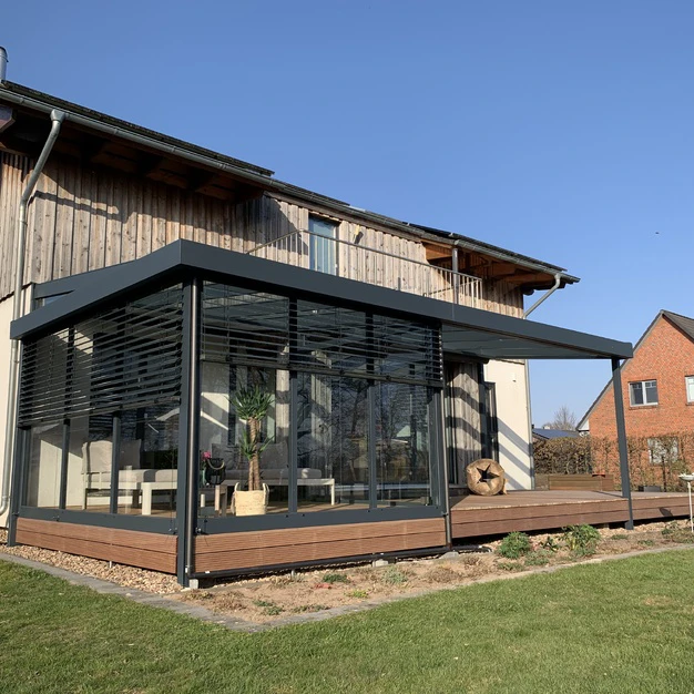 Moderne Glasverglasung als Wintergarten an einem Holzhaus mit Holzterrasse und Rasen