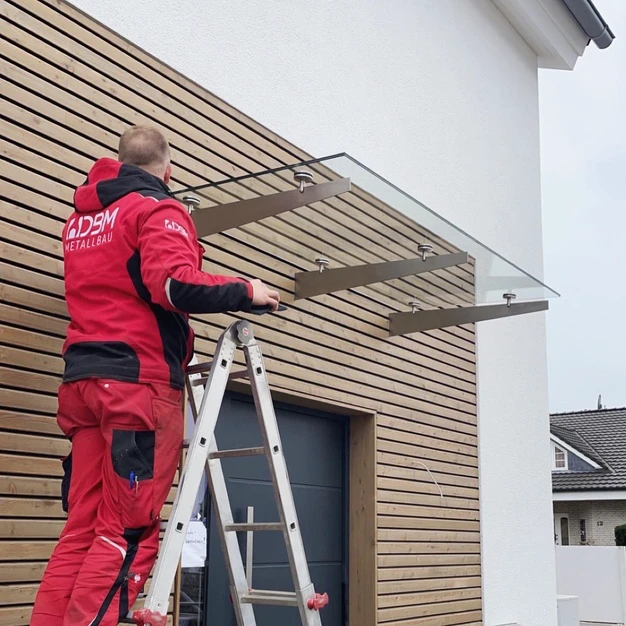 Mann installiert eine Glasbrüstung an einem modernen Haus mit Leiter und roten Arbeitskleidern