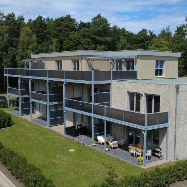Moderne Wohnhäuser mit Balkonen und heller Fassade umgeben von Wald und Grün
