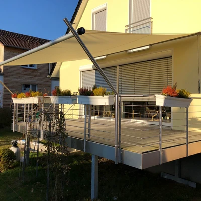 Balkon mit Sonnenschutz und gelbem Haus im Hintergrund