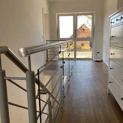 Modernes Treppenhaus mit Glasgeländer und hellem Holzparkett