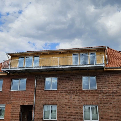 Backsteingebäude mit mehreren Fenstern und einem sichtbaren hölzernen Dachbalkon unter bewölktem Himmel