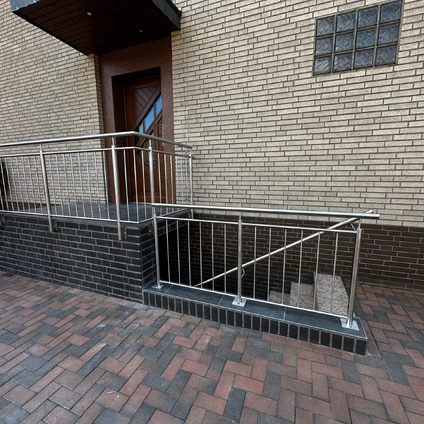 Ein Metallgeländer säumt die Treppe zu einem Eingangsportal an einer Backsteinwand