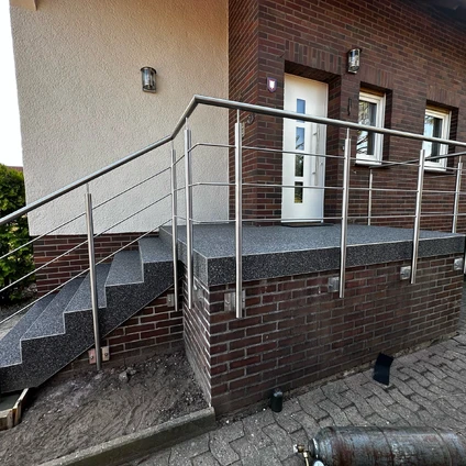 Eingangstreppe mit Metallgeländer und gemauertem Sockel vor beige-rotem Gebäude