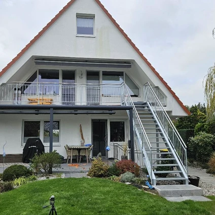 Zweistöckiges Haus mit weißer Fassade rotem Dach und externer Metalltreppe