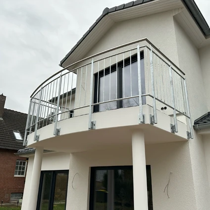 Geschwungener Balkon mit Metallgeländer an der modernen hellen Hausfassade unter bewölktem Himmel