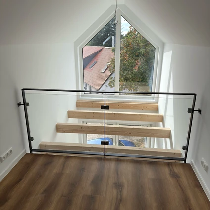 Modernes Treppengeländer aus Glas und Schwarzmetall vor einem großen dreieckigen Fenster mit Aussicht