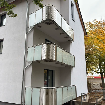 Moderne Wohnhausfassade mit drei Stockwerken und aneinandergereihten Glas- und Metallbalkonen