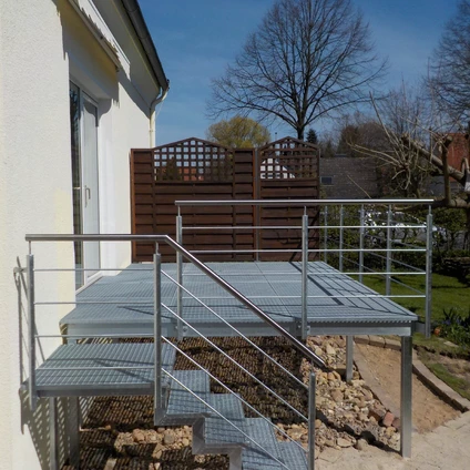 Moderne Metalltreppe mit Rampe vor einem Haus und braunem Holzzaun im Hintergrund