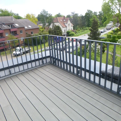 Blick vom Balkon auf eine grüne Wohngegend mit Häusern Bäumen und einer Straße