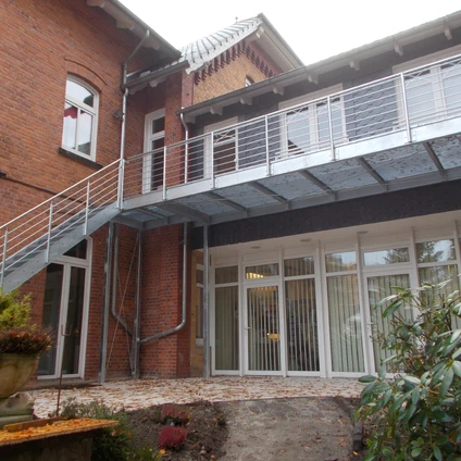 Backsteingebäude mit modernem Metallbalkon und großen hellen Fenstern im Erdgeschoss