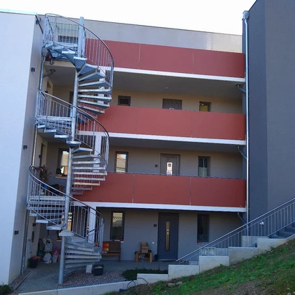 Modernes Wohngebäude mit orangenen Bändern weißer Fassade und markanter externer Spiraltreppe