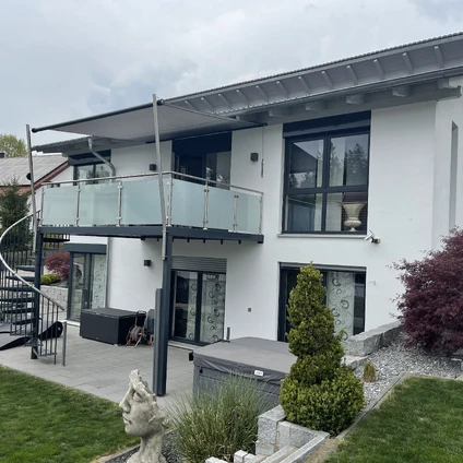 Modernes weißes Haus mit Glasbalkon großen schwarzen Fenstern und grüner Landschaftsgestaltung