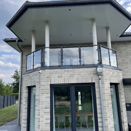 Modernes Wohnhaus mit hellen Ziegeln und einem großen überdachten Balkon mit Glasgeländer