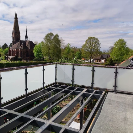 Dachgarten mit Zäunen im Vordergrund Blick auf eine historische Backsteinkirche und grünes Stadtpanorama