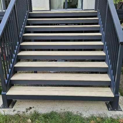 Moderne Außentreppe mit dunklen Metallgeländern und breiten hellen Holzstufen vor einem Haus