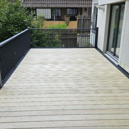Helles Holzdeck mit schwarzem Geländer Blick auf Grünpflanzen und moderne Architektur