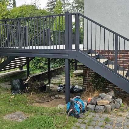 Graue Metalltreppenanlage und Steg im Außenbereich vor grünem gepflegtem Hintergrund