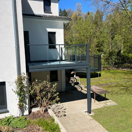 Modernes Wohnhaus mit Balkon und Glasgeländer vor grüner Naturkulisse und Rasen