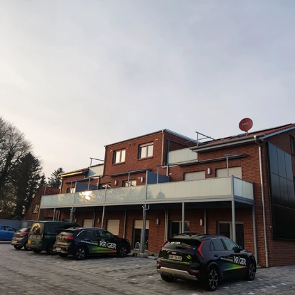 Dienstleistungsgebäude aus rotem Backstein mit geparkten Fahrzeugen vor der Fassade unter bewölktem Himmel