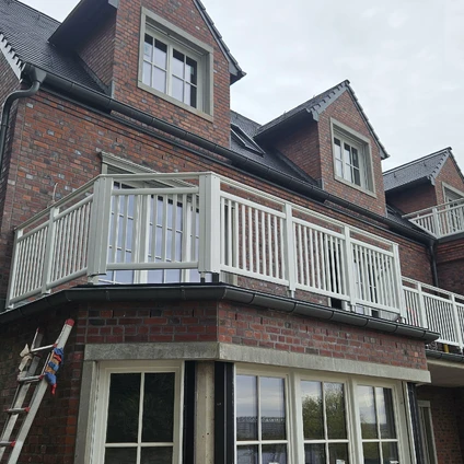 Red brick facade with a white enclosed balcony and dormer windows beneath a dark roof
