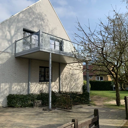 Modern Wohnhaus mit weißer Giebelfassade Balkon und umliegender Vegetation im Frühjahr