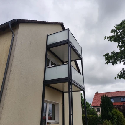 Moderne Hausfassade mit gestapelten vorspringenden Balkonen und Glasgeländern unter bewölktem Himmel