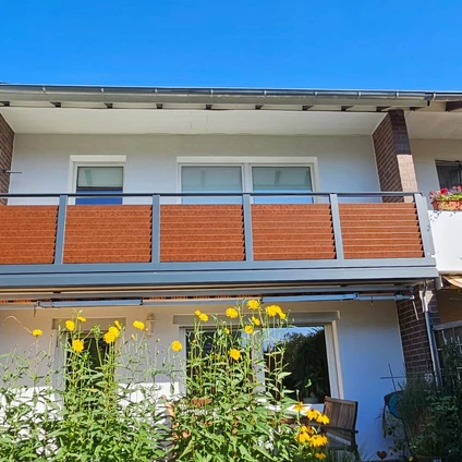 Zwei-Etagen-Haus mit Balkonen orangefarbenen Verkleidungen und blühenden gelben Blumen