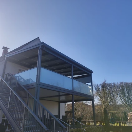 Moderne Struktur mit Metalltreppen und Glasgeländer unter blauem Himmel und Bäumen