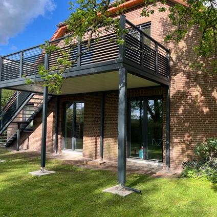 Balkon über dem Eingangsbereich gestützt von Metallstützen vor roter Ziegelmauer