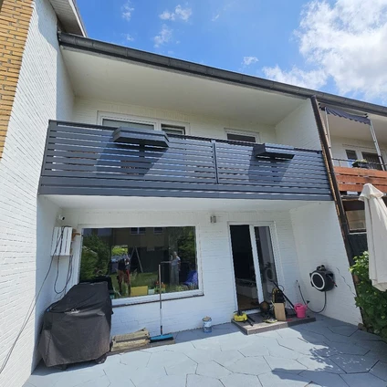 Modernes weißes Einfamilienhaus mit Balkon großen Fenstern und gepflasterter Terrasse