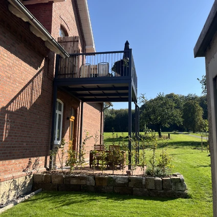 Backsteinghaus mit Balkon vor einer weiten grünen Wiesenlandschaft bei Sonnenschein