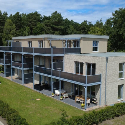 Modernes Haus mit Glasbalkonen vor einem grünen Waldhintergrund in ländlicher Umgebung