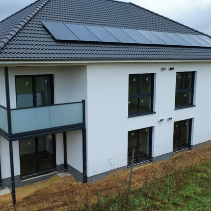 Modernes Haus mit Solarmodulen weißer Fassade und dunklen Fenstern auf einem Baugrundstück
