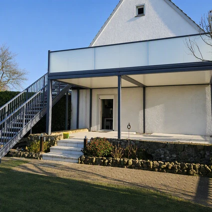 Modernes weißes Haus mit Vordach externer Metalltreppe und Steinsockel an einem sonnigen Tag