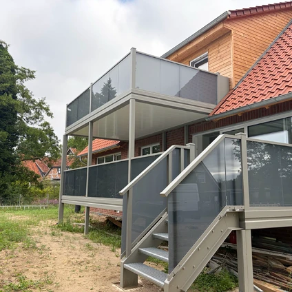 Moderne Anbaustruktur mit Treppe und Glasgeländern an ein Backsteinhaus im Garten