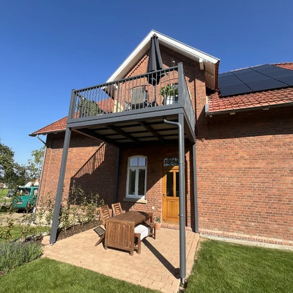 Backsteinhaus mit überdachtem Balkon Solaranlage und Gartenmöbeln an Sonnenschein
