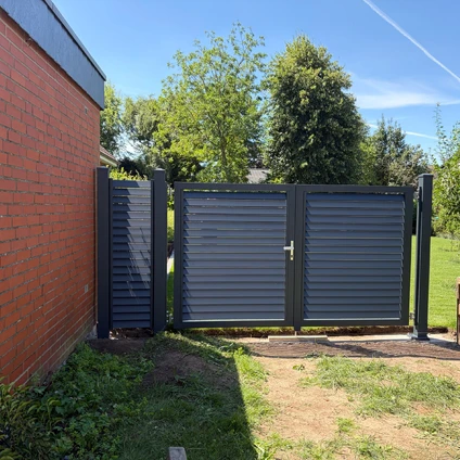Graue Schiebetore neben roter Ziegelwand vor grünem Garten und Bäumen unter blauem Himmel
