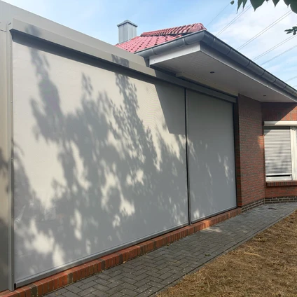Garage mit heller Tür und markanten Schattenwürfen eines Baumes auf dem gepflasterten Boden