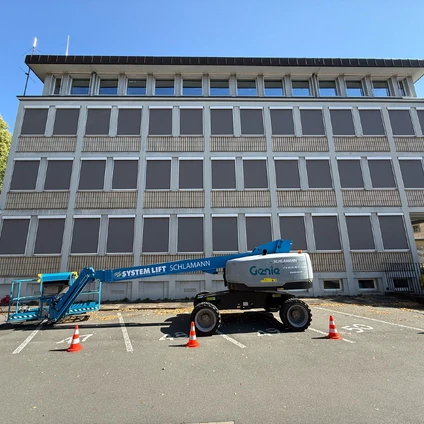 Gebäudefront mit vielen Fenstern und zwei Baumaschinen im Vordergrund